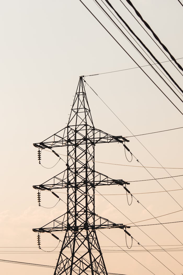 Silhouetted electric transmission tower against a dusk sky, showcasing power lines.